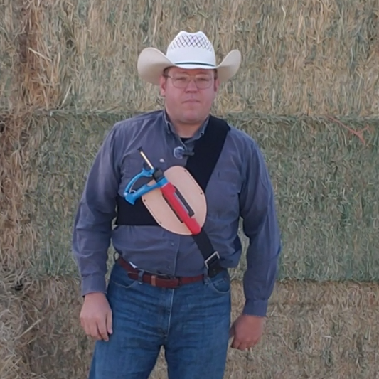 Man in cowboy hat and jeans standing in front of hay bales